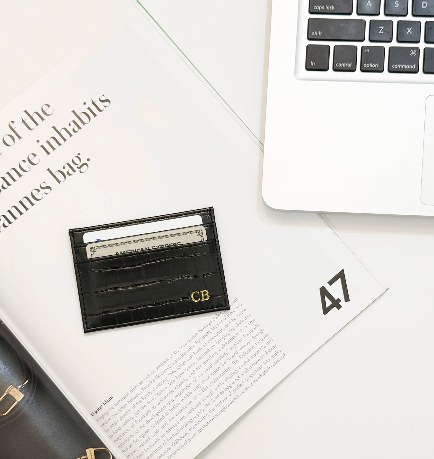 Black crocodile vegan leather cardholder laying on an open magazine by an open laptop