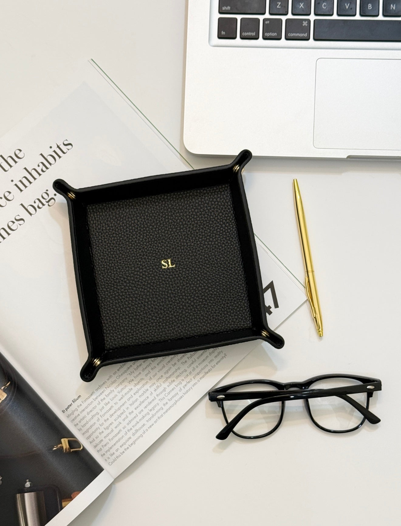 Monogrammed black valet tray by a gold pen, reading glasses, and a laptop