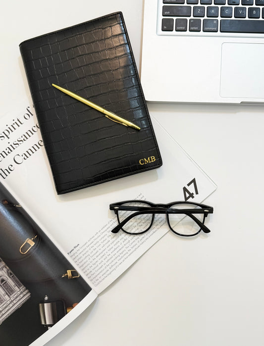 Monogrammed black croc notebook cover beside a pen and laptop