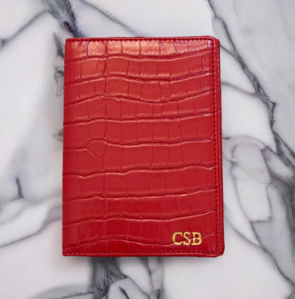 red croc passport cover with gold monogram at bottom right corner