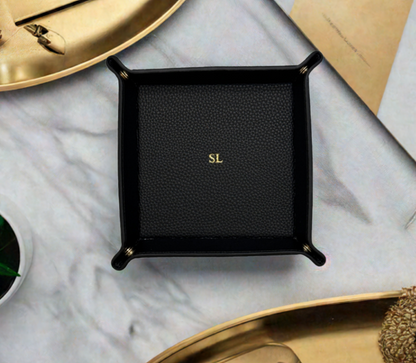 black monogrammed catchall tray surrounded by gold trays